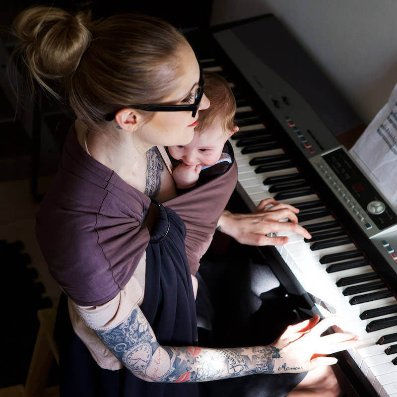 Mamma bär barn vid piano med Love Radius liten reversibel sjal antracit-kastanj
