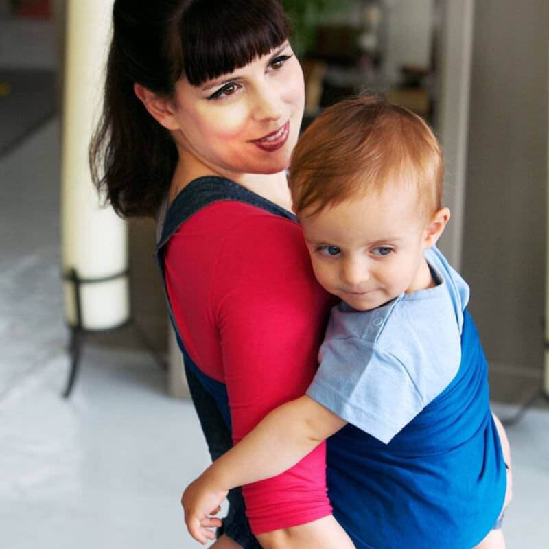 Mamma som bär sitt barn i den reversibla Love Radius Sling i blå och grå