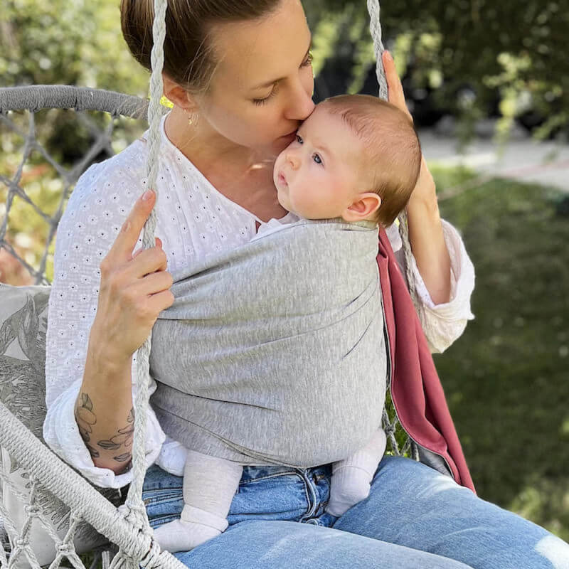 Mutter trägt Baby in reversible Love Radius Sling graumeliert im Garten