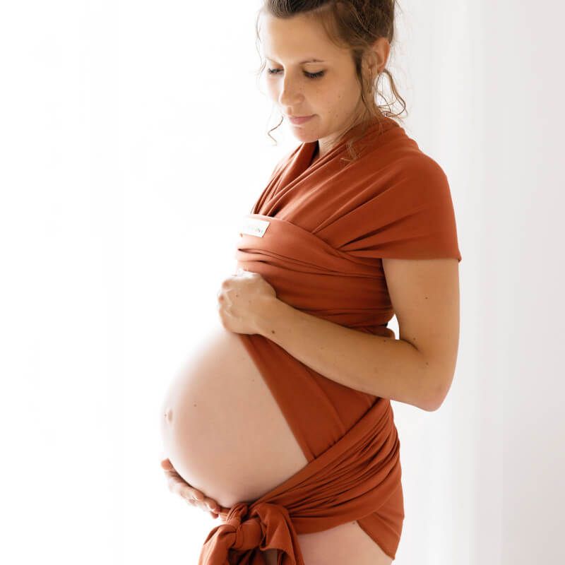 Zwangere vrouw in profiel draagt Love Radius BASIC draagsjaal fauve om haar buik gewikkeld