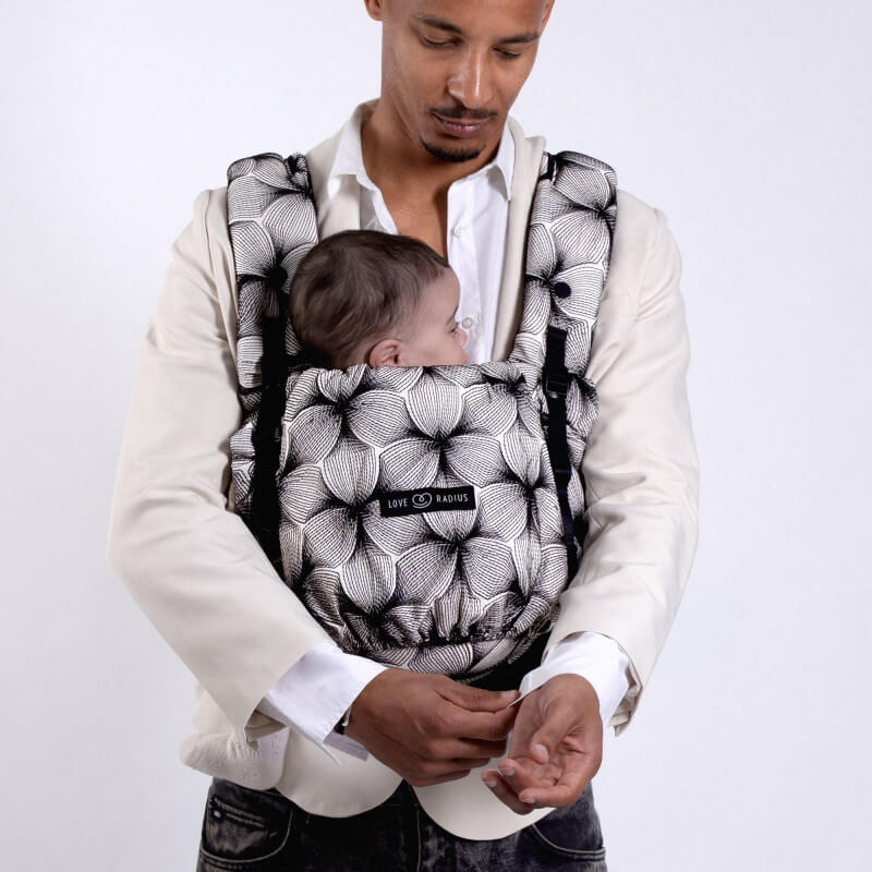 Padre che indossa il Love Radius PhysioCarrier 2 con neonato in posizione ventrale, motivo nero