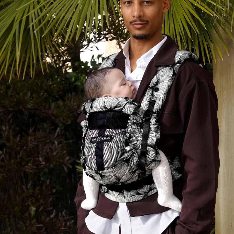 Padre che indossa neonato in Love Radius PhysioCarrier 2 con motivo foglie, esterno tropicale