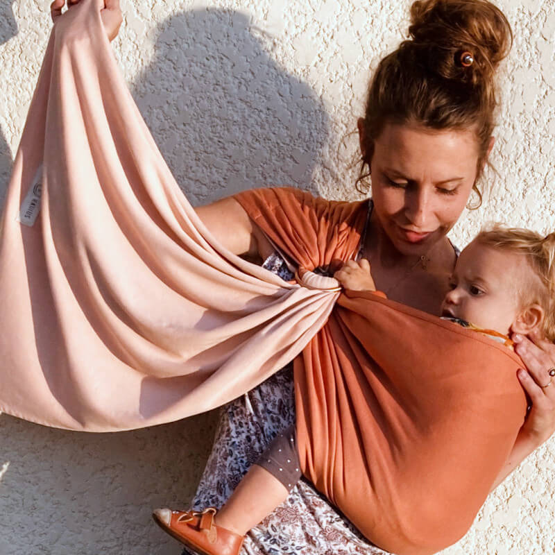 Love Radius Sling umlegbar Nude Caramel mit Kind an strukturierter weißer Wand