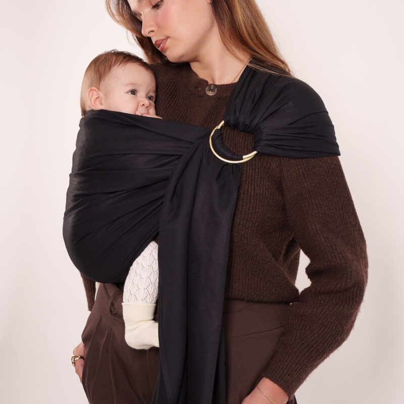 Madre che porta il suo bambino con la fascia portabebè Love Radius nera, chiusura ad anello dorato