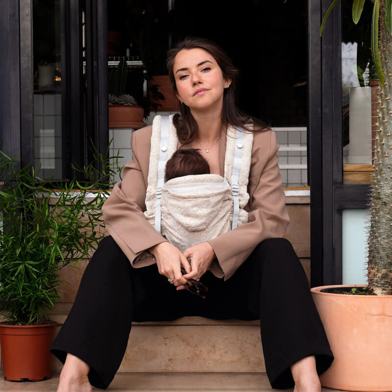 Mujer con portabebés Love Radius HoodieCarrier 2 lino, sentada en terraza exterior