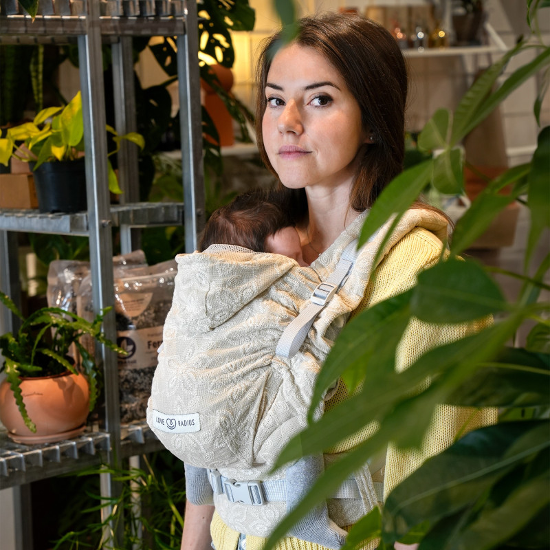Love Radius HoodieCarrier 2 Fleur di Lino, donna che indossa il bebè circondato da piante verdi