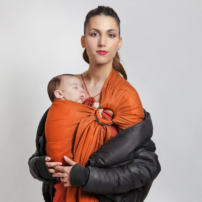 Vrouw draagt baby in Love Radius Sling Geweven Draagdoek in tawny
