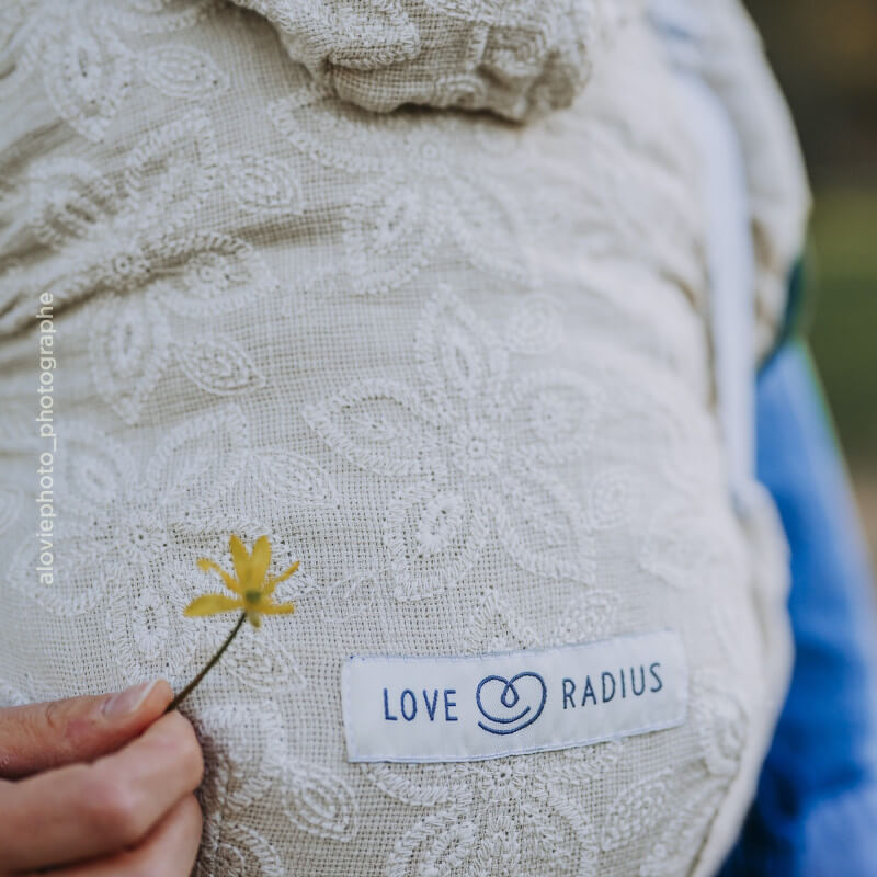 Portabebés Love Radius HoodieCarrier 2 en lino crudo, detalle de textura jacquard y etiqueta de marca