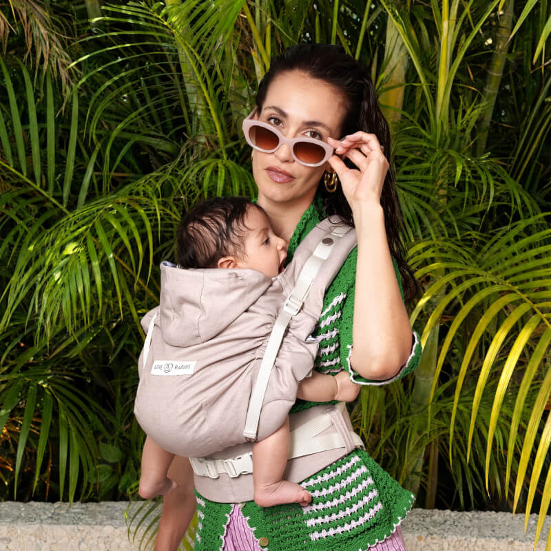 Madre che indossa il neonato nel marsupio Love Radius HoodieCarrier 2 beige, sfondo tropicale